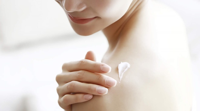 Woman applying body moisturizer on shoulder